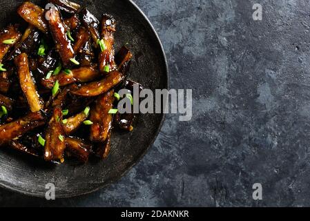 Nahaufnahme der Brut Bulgogi Aubergine auf Platte über dunklen Stein Hintergrund mit freien Text Raum. Gebratene Aubergine im koreanischen Stil. Draufsicht, flach l Stockfoto
