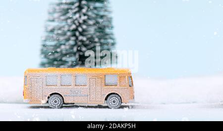 Weihnachts- oder Neujahrskomposition, Dekoration mit Glaskugel Schneekugel, gelbem Bus und Tannenbaum mit Schnee bedeckt auf Glitzerhintergrund Stockfoto