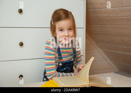 Kleines Mädchen sitzt an einem Tisch und blättert durch ein Buchen Stockfoto