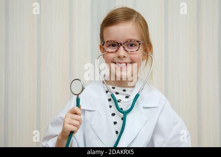 Ein kleines Mädchen im Arztmantel lächelt und lädt zur Behandlung ein. Pädagogische medizinische Spiel. Stockfoto