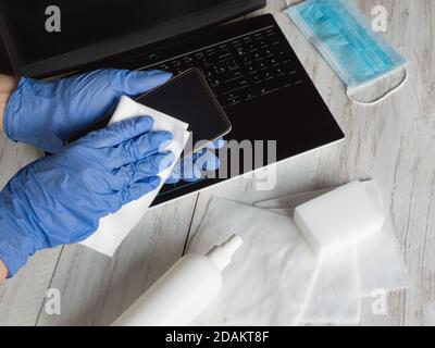 Hände in blauen Handschuhen wischen Smartphone-Bildschirm mit Desinfektionsmittel Tuch von Bakterien und Viren. Stockfoto