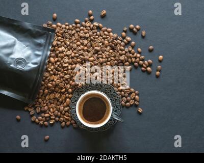 Kaffeebohnen verschüttet aus einer Packung auf einem schwarzen Tisch. Stockfoto