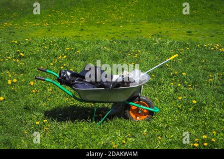 Wagen mit Müll auf dem grünen Gras. Reinigung des Parks nach einem Grill in der Natur. Stockfoto