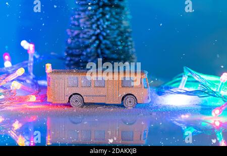 Miniatur gelben Bus und Tannenbaum während Schneefall, Nachahmung der Nachtzeit mit Girlande. Weihnachtsdekoration, Weihnachtskarte mit Platz für Text Stockfoto
