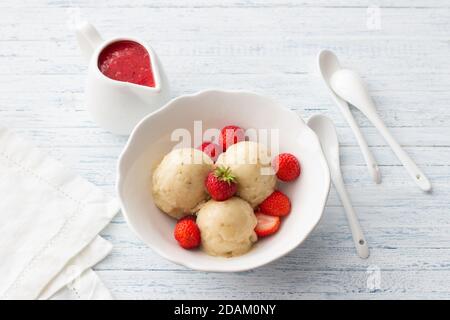 Veganes Bananeneis mit Erdbeersoße und frischen Erdbeeren In einer weißen Schale auf hellblauem Holzhintergrund Stockfoto
