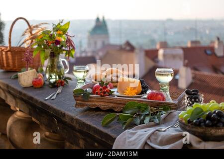 Käse, Äpfel und andere Speisen auf einem Tablett auf einem Balkon, mit einem Panorama von Prag im Hintergrund Stockfoto