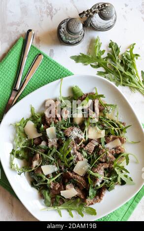 Fleischstreifen mit Rucola und Parmesan auf einem weißen Teller. Draufsicht. Stockfoto