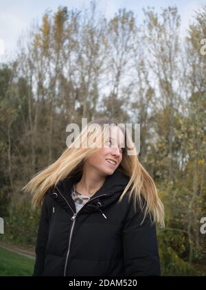 Schöne junge Frau wirft ihr langes blondes Haar im Herbst Parken Stockfoto