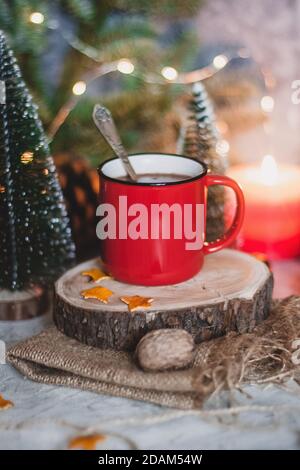 Gemütlicher Wintertrunk heißer Schokoladenkakao in rotem Becher mit Tannenbaum, Kerzen und Weihnachtsbeleuchtung Stockfoto