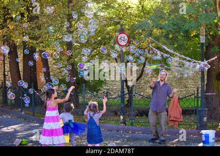 Krakau, Polen - 12. Oktober 2019: Ein Mann bläst Wasserblase umgeben von Kindern in einem grünen Park. Freizeitaktivitäten für die Familie am Wochenende Stockfoto