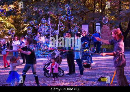 Krakau, Polen - 12. Oktober 2019: Ein Mann bläst Wasserblase umgeben von Kindern in einem grünen Park. Freizeitaktivitäten für die Familie am Wochenende Stockfoto