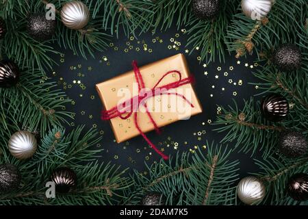 Weihnachtsgeschenk mit Kugel Draufsicht. Christbaumzweige, Zapfen und Kugeln auf schwarzem Hintergrund. Stilvolle Dekorelemente für Neujahr. Stockfoto