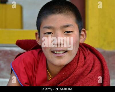 Freundliche Pre-teen tibetischen buddhistischen Jungen Mönch trägt traditionelle kastanienbraun Kleidung und lächelt für die Kamera. Stockfoto