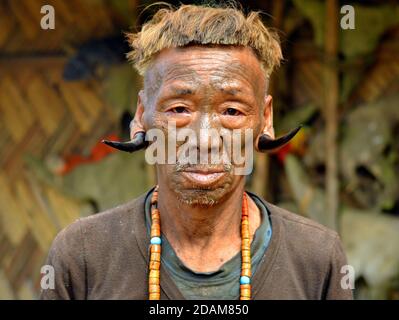 Alter Konyak Naga Krieger und Ex-Headhunter mit Gesichts-Tattoo, Tribal Frisur und Hirsch Hörner in den Ohrläppchen Posen für die Kamera (Frontalfoto). Stockfoto