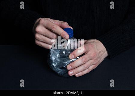 Mann zerschlug eine Plastikflasche mit den Händen auf schwarz Hintergrund Stockfoto