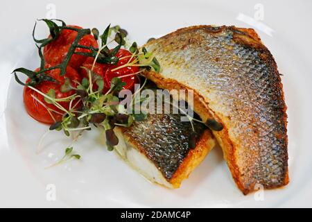 Gebratenes Fischfilet vom Grill mit Tomaten und Kräutern Auf einem weißen Teller Stockfoto