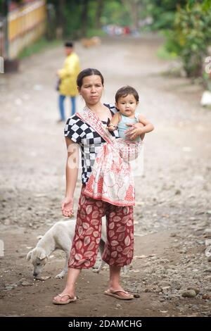 Indonesische Frau auf der Straße hält Kind in einem Wrap auf einer Seite. Lombok, Indonesien. Stockfoto