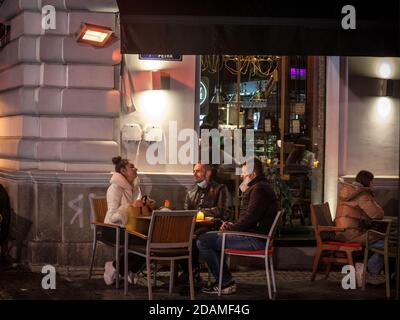 BELGRAD, SERBIEN - 20. OKTOBER 2020: Drei Freunde, Gäste in der Nacht auf einer beheizten Terrasse eines Cafés serviert Essen und Trinken trägt ein Atemgesicht m Stockfoto