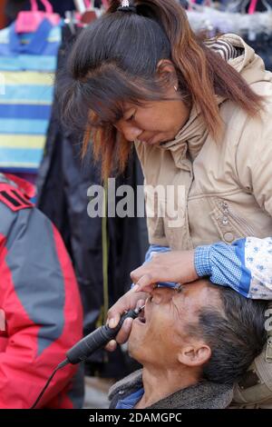 Weibliche „Zahnärztin“ auf dem Land, bohrende Zähne von grimmigen Patienten auf der Straße, am Markttag in Wumulong, Yongde County, Lincang, Yunnan, China, Januar 2013 Stockfoto