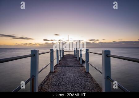 Blick über einen Pier auf das Meer, ein lila Abendlicht Horizont Himmel Stockfoto