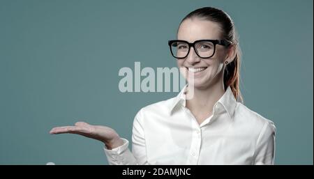 Selbstbewusste junge Geschäftsfrau, die der Kamera etwas zeigt und lächelt Stockfoto