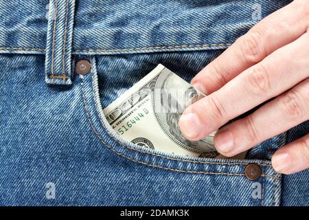 Hand nimmt US-Dollar Banknote aus der rechten Vordertasche der blauen Jeans. Konzept der Einsparung von Geld oder Taschenkosten Stockfoto