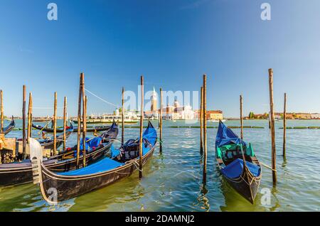 Gondeln, die in Venedig an Wasser angedockt sind. Gondoliere segeln San Marco Wasserlauf. Insel San Giorgio Maggiore mit Campanile San Giorgio in Vene Stockfoto