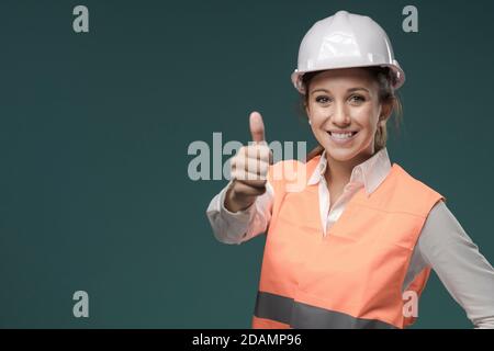 Lächelnde junge Frau trägt eine Sicherheitsweste und Schutzhelm, Sicherheit am Arbeitsplatz und Schutz Arbeitskleidung Konzept Stockfoto