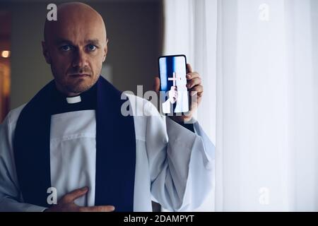 Junger Priester mit Mobiltelefon. Stockfoto