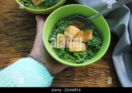 Frauen Hand hält frische und leckere grüne Suppe . Schüssel Brokkoli mit Croutons. Diät Detox Food Konzept. Draufsicht, flach liegend Stockfoto