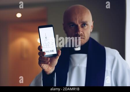 Junger Priester hält ein Handy mit Informationen für Christen. Stockfoto