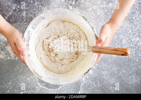 Nahaufnahme der Hände halten eine Glasschale mit Teig. Einen köstlichen Teig mit Mehl, Eiern, Milch und Zucker verquirlen. Der Teig ist fertig zum Kochen. Stockfoto