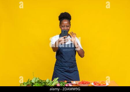 Weibliche afrikanische Köchin macht einen Videoanruf, Wellen an ihrem Telefon Stockfoto