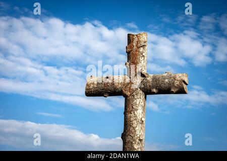 Altes christliches Kreuz aus Stein am blauen Himmel mit Wolken (Nachahmung eines Baumstammes), in der Nähe des kleinen Dorfes Sant'Anna d'Alfaedo, Italien. Stockfoto