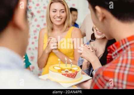 Glücksmoment Geburtstagskuchen mit Kerze Frau und Freunde genießen lächelnd, selektive Fokus auf Geburtstagskuchen Kerze. Stockfoto