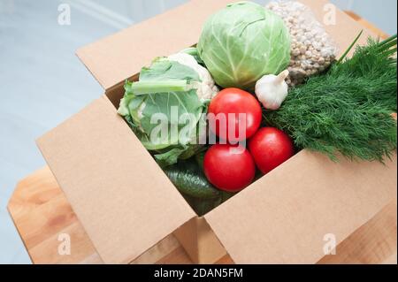 Kontaktlose Produktlieferung an der Tür. Lebensmittelspende Paket Gemüse, um die Kranken oder Armen zu helfen. Donat-Box mit Lebensmitteln Stockfoto