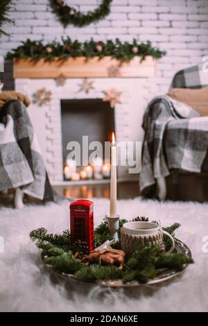 Eine Tasse heißen Kräutertee auf einem eisernen Tablett mit Christbaumzweigen, brennenden Kerzen, Zapfen, Keksen, Spielzeug. Weihnachten Hintergrund. Neujahr Stockfoto