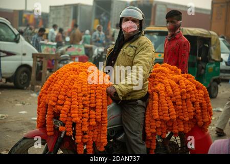 Neu Delhi, Indien. November 2020. Ein Mann, der eine Maske trägt, trägt Girlanden von Ringelblumen auf einem Motorrad. Ein Großhandel Blumenmarkt in Neu Delhi während Covid-19 Pandemie. Blumen sind wichtig in hinduistischen Festivals für Dekoration und Opfergaben an Gottheiten. Kredit: SOPA Images Limited/Alamy Live Nachrichten Stockfoto