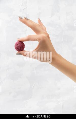 Bunte vegane Süßigkeiten Energie Ball auf Womans Hand auf grau Hintergrund Stockfoto