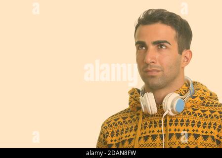 Junger, hübscher Iraner, der beim Denken Kopfhörer um den Hals trägt Stockfoto