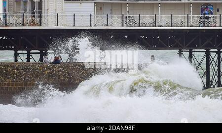 Brighton UK 14. November 2020 - Wellen krachen über der Strandpromenade von Brighton und Besucher können sich an einem windigen Tag an der Südküste entspannen : Credit Simon Dack / Alamy Live News Stockfoto