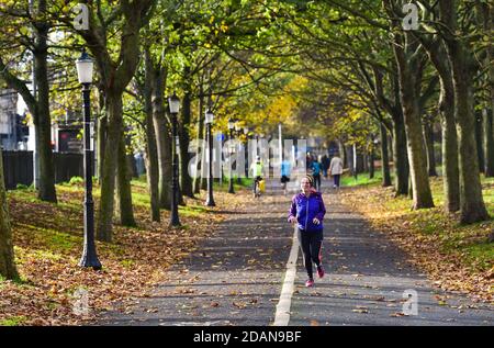 Brighton UK 14. November 2020 - EIN Läufer macht das Beste aus einem Blick auf die Sonne auf dem Level in Brighton, während nasses und windiges Wetter entlang der Südküste fegt : Credit Simon Dack / Alamy Live News Stockfoto