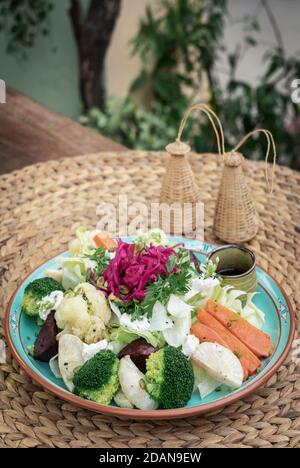 Rustikaler Hüttensalat mit gesundem, gedünstetem und frischem Gemüse Auf buntem Teller im Garten Stockfoto