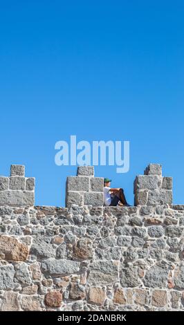 Junger Mann sitzt und klettert die Wand eines Schlosses Mit Kopierplatz an einem blauen und sonnigen Tag Stockfoto