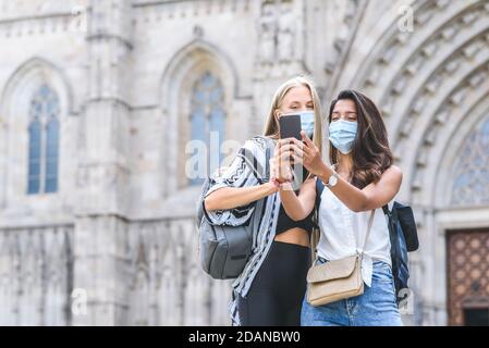 kaukasische und indische Freundinnen mit Smartphone zu nehmen Selbst ein Bild mit der Kathedrale von Barcelona im Hintergrund Stockfoto