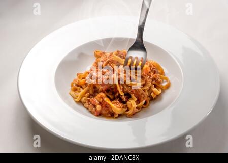 Spaghetti auf Ei-Basis (italienische Tagliatelle) mit Fleisch und Tomatensauce Whit Gabel gekrönt, gedämpft in einem Teller auf weißem Hintergrund Stockfoto