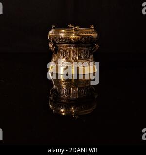 Verzierte Bronze Ornament auf einer glänzend schwarzen reflektierenden Oberfläche, zeigt ein invertiertes Spiegelbild. Stockfoto