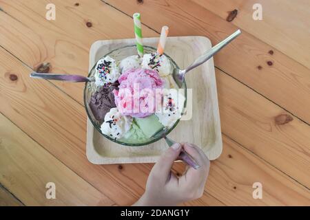 Kind hält Löffel essen Eis verschiedene Farben und Geschmacksrichtungen in Schüssel auf Holz Tischplatte. Selektiver Fokus Stockfoto