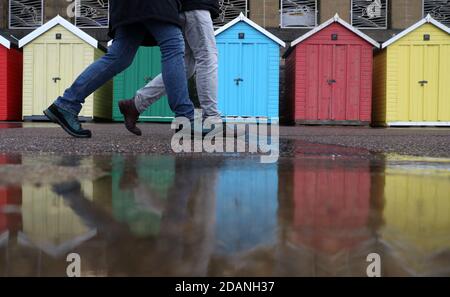 Die Leute laufen an Strandhütten am Meer neben dem Strand von Boscombe in Dorset vorbei. Stockfoto