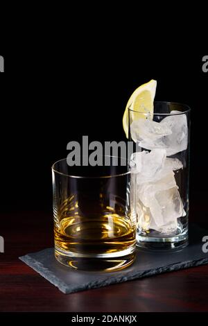 Whiskey ordentlich und ein Glas Eis auf Schieferplatte serviert. Dunkelroter Holztisch, hohe Auflösung Stockfoto